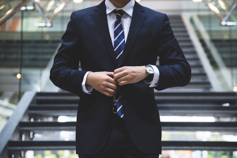 Person in a suit adjusting their jacket while standing in front of a staircase.